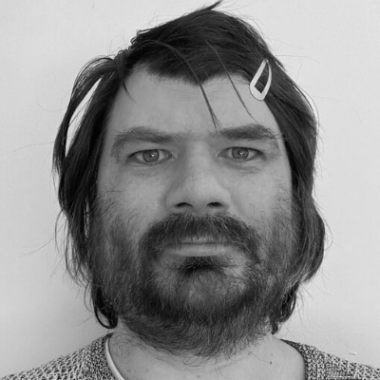 A person with dark beard and facial hair looking at the camera.