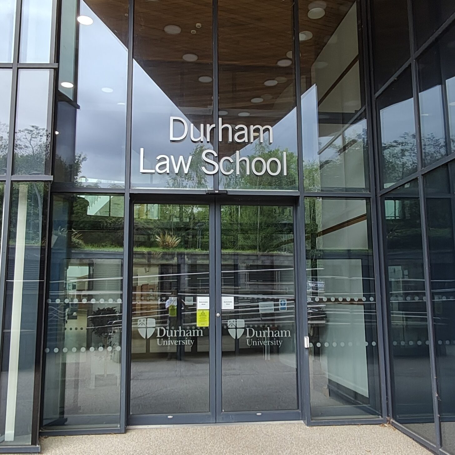 Pair of glass automatic doors with a sign reading "Durham Law School" above them.